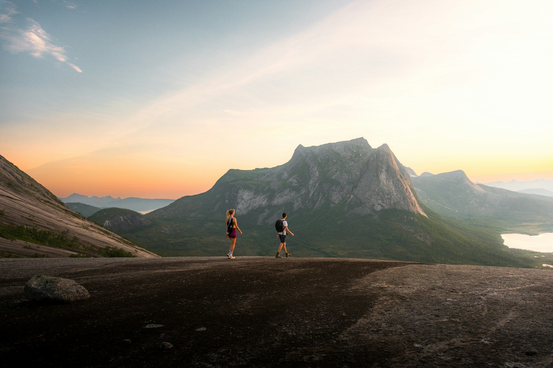 Two people standing on a mountain trail at sunset with a large mountain in the background.